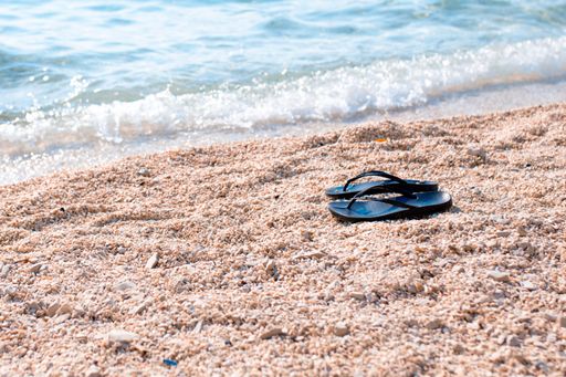 A pair of black flip flop sandals lying on the sandy beach near water