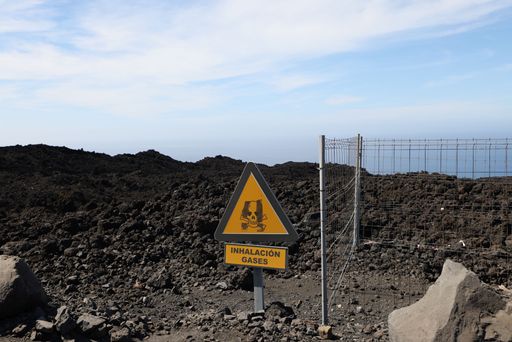 A yellow warning sign "Volcano Attention gases" in the lava on La Palma