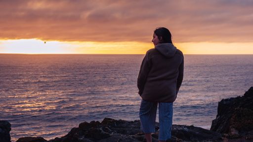 woman watching a sunset on the beach, the sun setting in the se. 
Chile Cold day