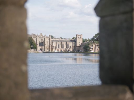 A view of Newstead Abbey, a historic estate located in Nottinghamshire, England, seen through a stone arch window across the lake