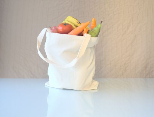A reusable textile tote bag full of vegetables and fruits on white table