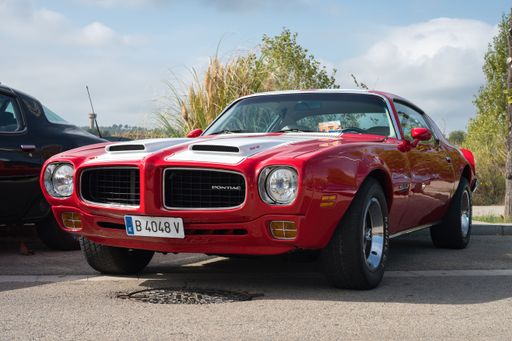 Front view of a classic red American sports muscle car with white stripes parked on the street, it is a second generation Pontiac Firebird Formula 400
