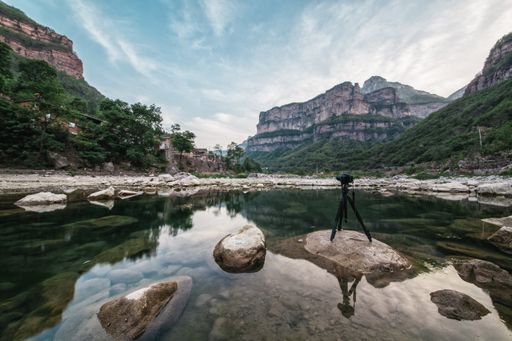 A camera with a tripod on the rock of a river capturing the beautiful landscape of mountains