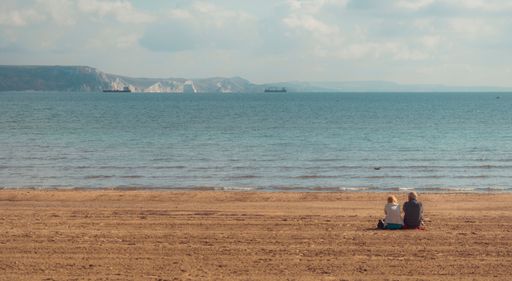 A man and a woman sitting on a beach and looking at the peaceful sea