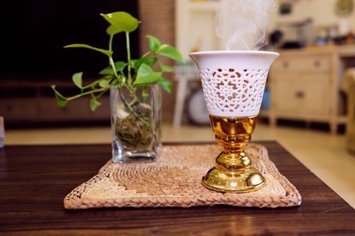 A white ceramic cup with a smoky aroma emitting from its surface sits atop a wooden table next to a green houseplant