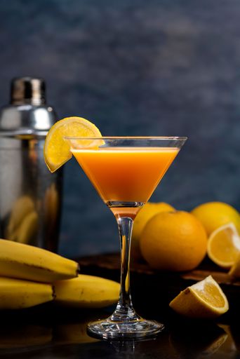 A close up view of a cocktail glass filled with orange juice, fresh oranges, and bananas