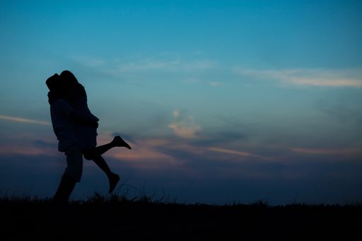 A silhouette of a couple hugging each other on a blue sky background