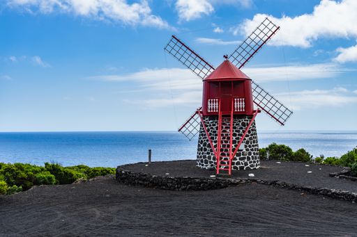 A red windmill on Pico coastline with blue clear sky in Azores