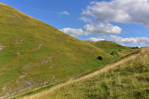 A scenic view of green hills under a cloudy blue sky on a sunny day