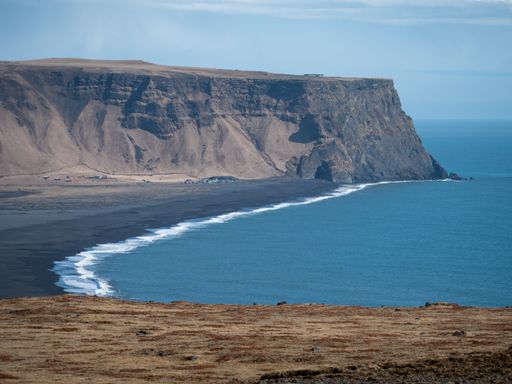 A stunning view of a large rocky cliff face, with a sparsely vegetated landscape, overlooking a vast expanse of sparkling blue ocean