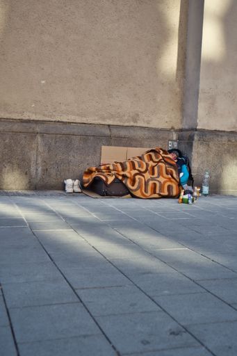 A homeless man lies in his sleeping bag on the street. Many beggars in the center of munich.
