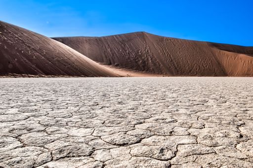 A vast, sun-drenched desert landscape under a clear, blue sky, Sossusvlei, Namibia