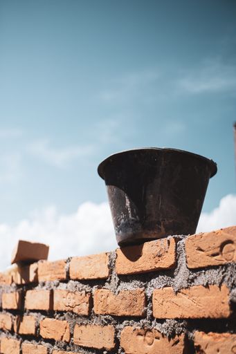 A vertical shot of a mason bucket with cement on a brick wall
