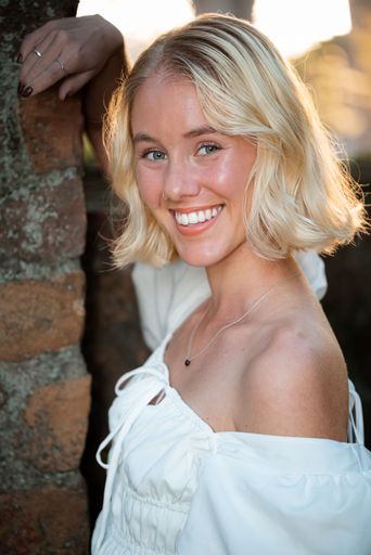 A young, attractive Caucasian blonde female smiling and posing in a white dress