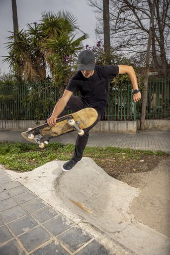 A young caucasian male from Italy in a black shirt and cap jumping with his skateboard