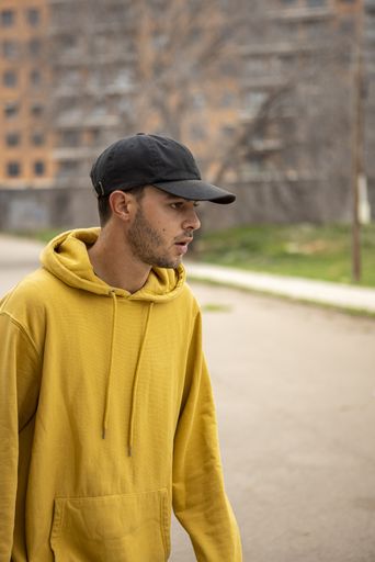 a young caucasian male from Italy in a yellow hoodie and black cap standing on the street