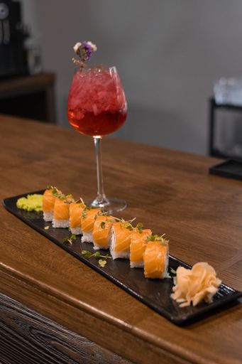 A vertical shot of appetizing salmon sushi rolls on a plate served with a berry cocktail