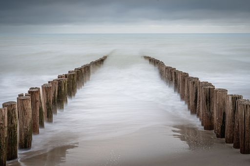 A tranquil coastal landscape featuring aged wooden logs on the shoreline of a sandy beach, with waves lapping at the shore