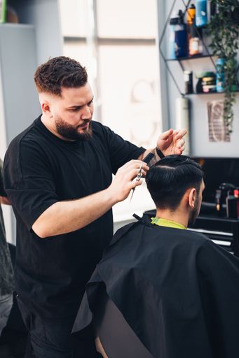 A vertical of a barber trimming a male customer's hair in a salon