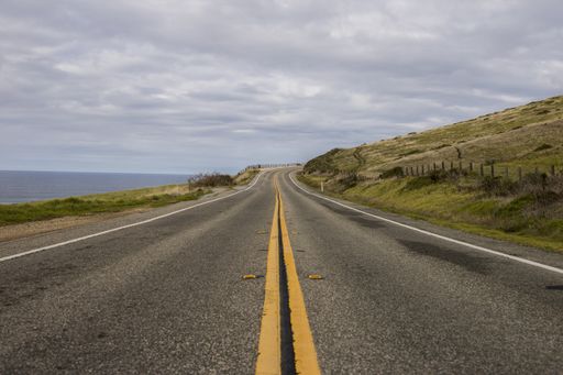 A beautiful shot of an asphalt road surrounded by mountains and the ocean on a cloudy day