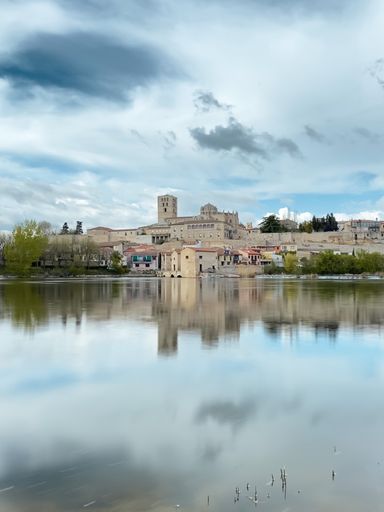 A scenic view of a calm sea with the reflection of the Catedral de Zamora on the surface