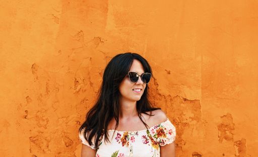 A closeup shot of a beautiful Caucasian woman with sunglasses on the orange wall background