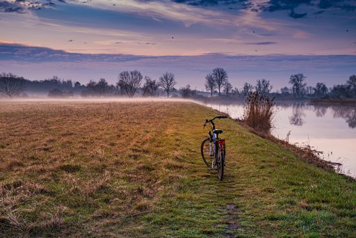 A beautiful shot of a bicycle in the field near a lake over the cloudy sky
