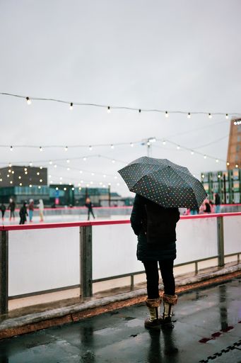 A person holding an umbrella standing next to a skating court on a cloudy day in Copenhagen, Denmark.