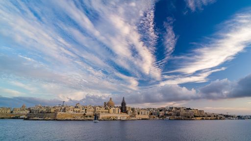A cityscape of Valletta surrounded by the sea under a blue cloudy sky in Malta