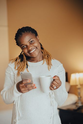 A happy African female enjoying a cup of coffee while using her phone