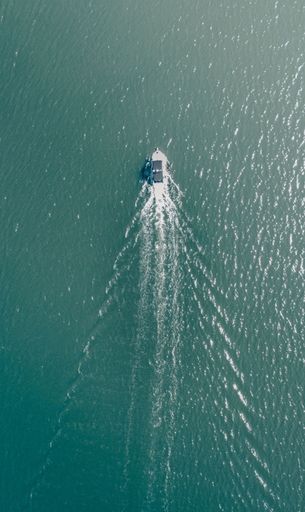 Aerial view of a small boat floating in a tranquil body of clear blue water with gentle ripples on the surface
