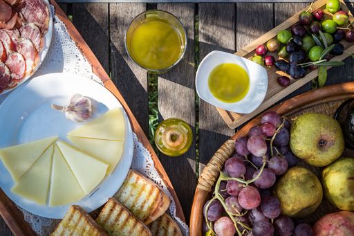 A top view of a wooden table with delicious Mediterranean cuisine including olive oil, salami, and cheese