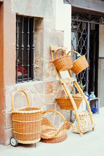 A vertical shot of straw baskets of different shapes on street near a stone wall for sale