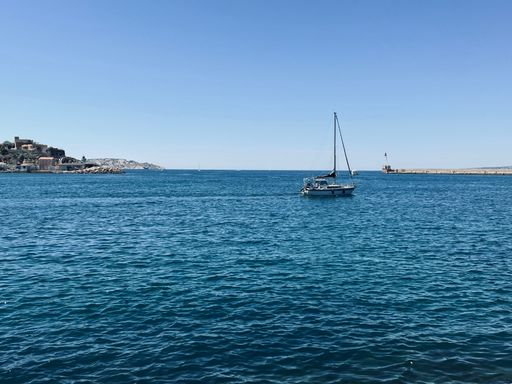 A small fishing boat sailing in the middle of a vast ocean, with a tropical island in the background