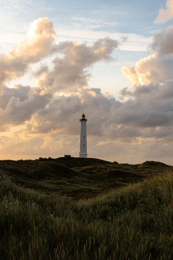 An idyllic scene of a majestic lighthouse perched atop a grassy hill overlooking the ocean
