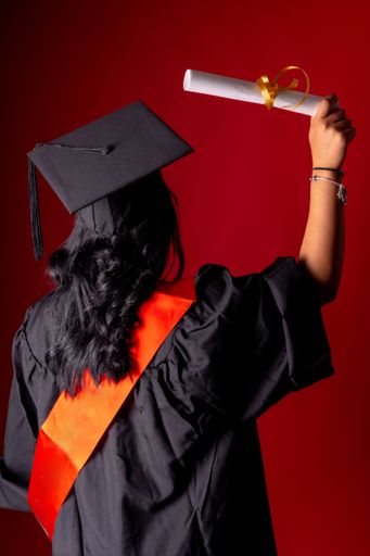 A young adult proudly displays their newly acquired diploma while wearing a black graduation gown with gold trim