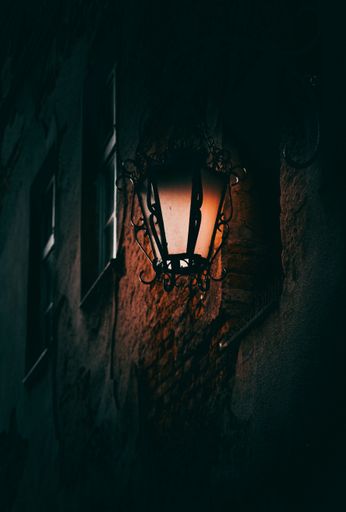 A vertical shot of an illuminated street lamp on the wall of an old building at night