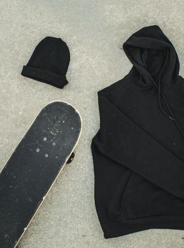 An image of a black beanie and skateboard lying atop a black clothing item on a plain background