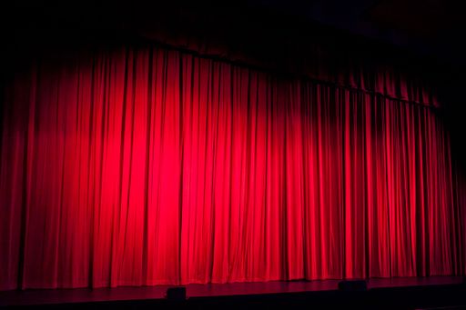 An illuminated theatrical stage with a voluminous draped red curtain