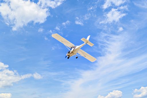 A low angle shot of a Single engine ultralight plane flying in the blue sky with white clouds