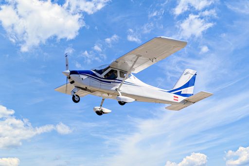 A low angle shot of a Single engine ultralight plane flying in the blue sky with white clouds