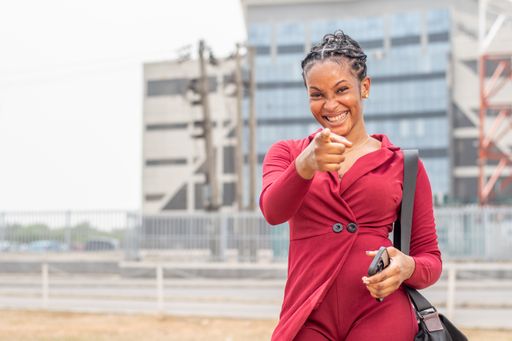 A smiling young beautiful African lady points at the camera.