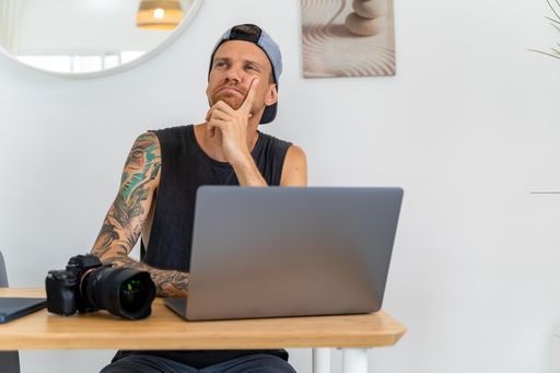 A male is sitting at a desk with laptop and thinking