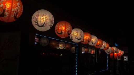 A row of bright Japanese lanterns hanging from the ceiling in a dark room