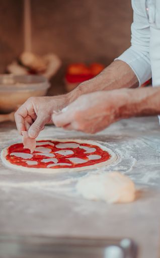 A vertical closeup shot of male hands in the pizza-making process