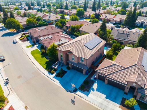 Aerial view of suburban residential area featuring a wide paved street surrounded by multiple homes with brightly colored roofs