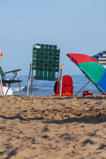 A selective focus on a green deck chair and beach elements, with the sea in the background. Vacation concept.