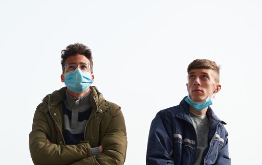 A closeup of two young Caucasian and Hispanic guys wearing sanitary masks outdoors