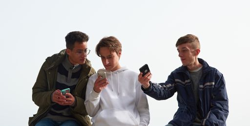 A closeup of three young Caucasian and Hispanic guys socializing and using their smartphones