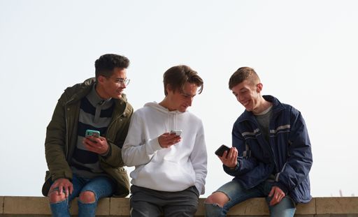 A closeup of three young Caucasian and Hispanic guys socializing and using their smartphones